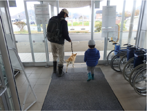 お父さんと子供が、茶色の犬を連れて出口から出ていく